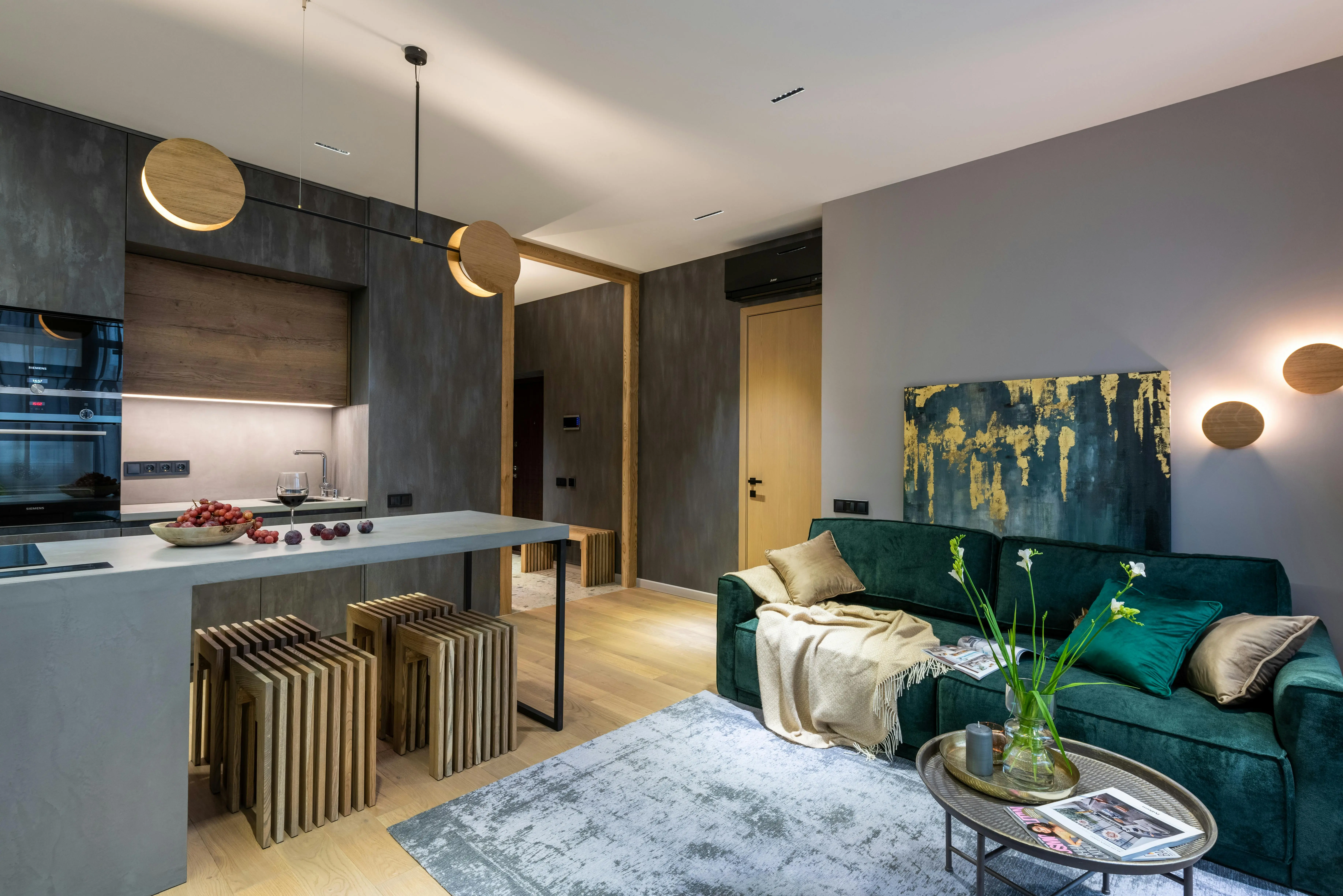 Contemporary open-plan apartment with a green velvet sofa, golden wall art, modern lighting, and a sleek kitchen island, highlighting elegant home design trends in online furniture retail